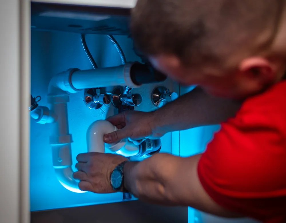 Technician working on plumbing inside a cabinet under a sink